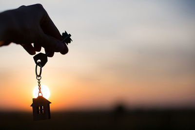 Silhouette of a house figure with a key, a pen with a keychain on the background of the sunset. 