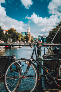 Bicycle parked on bridge over river against cloudy sky in city