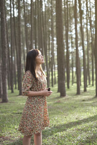 Full length of woman standing by tree trunk in forest