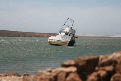 Abandoned sailboat on sea shore against sky