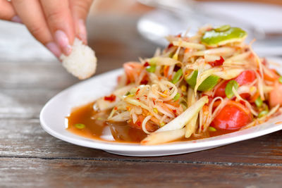 Close-up of hand holding food in plate on table