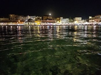 Illuminated cityscape by river against sky at night