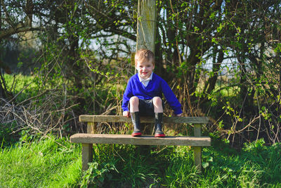 Portrait of cute boy sitting on bench against trees