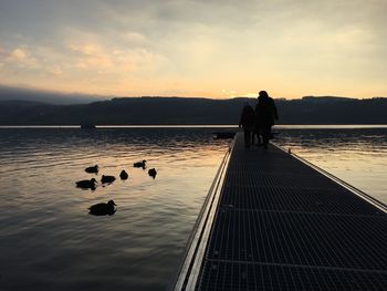 Silhouette people on pier over lake during sunset