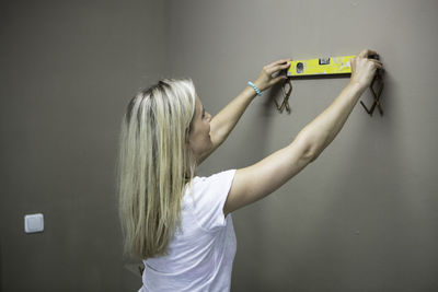 Side view of woman holding level with coat hooks on brown wall