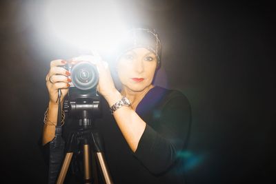 Portrait of woman photographing against black background