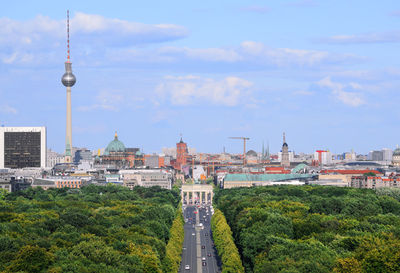 Communications tower in city against cloudy sky