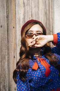 Portrait of woman wearing sunglasses standing against wall outdoors