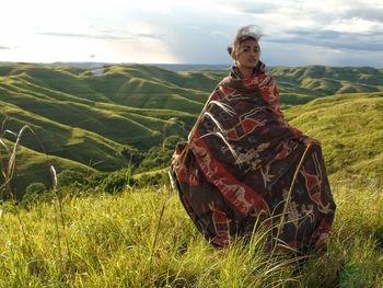 Portrait of young woman wearing shawl on grassy mountain against sky