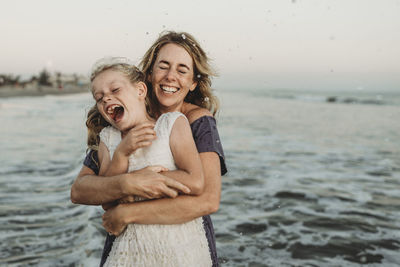 Mother embracing young girl with freckles in ocean