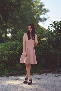 Smiling beautiful woman standing on sand against plants