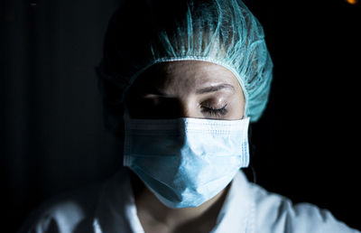 Portrait of young female surgeon, wearing mask and a surgical mask, in front of black background