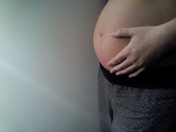 Midsection of pregnant woman touching her belly against wall
