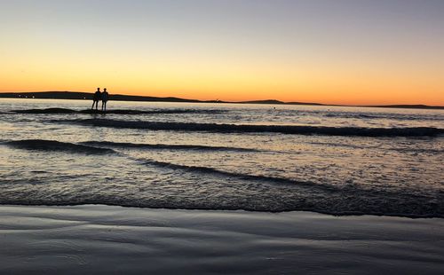 Silhouette people in sea against sky during sunset