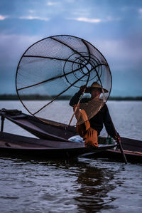 Man standing on fishing boat in lake against sky