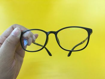 Close-up of human hand holding eyeglasses against yellow background