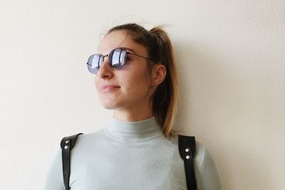 Close-up portrait of young woman with eyeglasses against wall