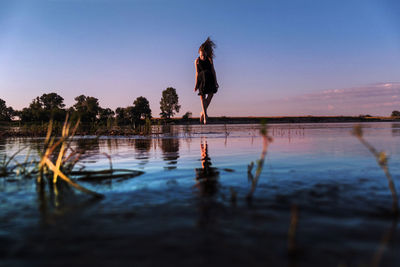 Full length of girl jumping in lake against sky during sunset