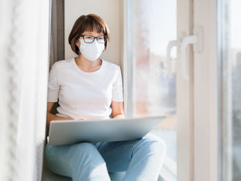 Pretty woman in medical mask works remotely from home.