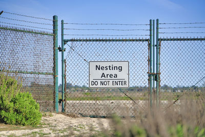 Information sign on fence by field against sky