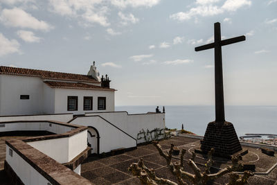 Cross by sea against buildings against sky