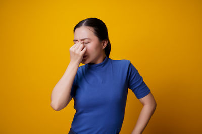 Young woman standing against yellow background