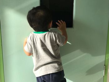 Rear view of boy standing against wall at home