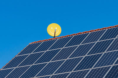 Satellite dish with a painted smile on the roof of a house. solar panels on the roof. clear blue sky