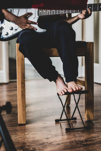 Low section of man playing guitar while sitting on chair at home