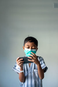 Portrait of boy holding mobile phone against wall