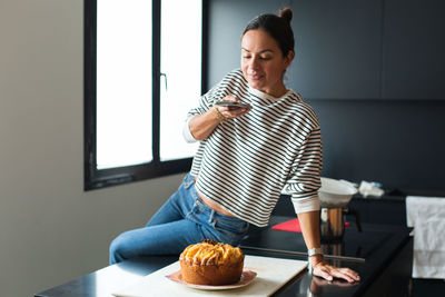 Woman making a photo for a social media on her phone while cooking apple pie in the modern kitchen