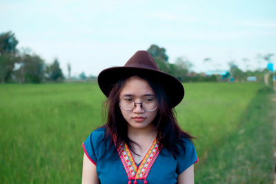 Thoughtful young woman wearing hat looking down on field