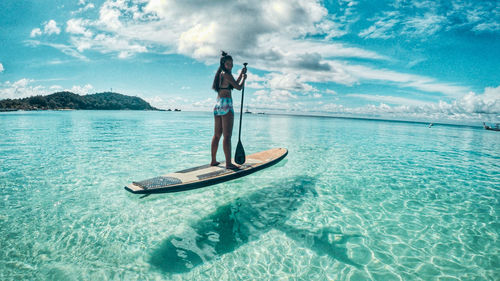 Woman standing in sea against sky-paddle boarding