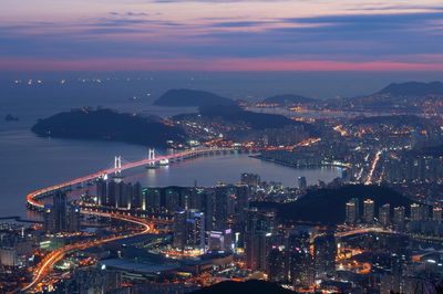 Aerial view of gwangandaegyo over sea by illuminated cityscape during sunset