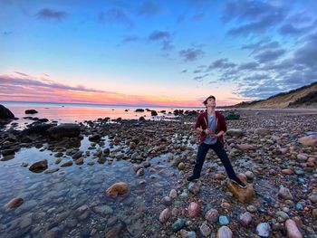 Full length of man on rocks at beach during sunset