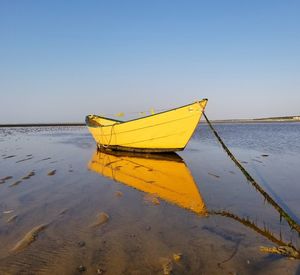 Yellow boat moored on beach against clear sky