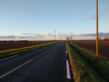 Empty road amidst field against sky