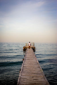 Man walking on pier over sea against sky