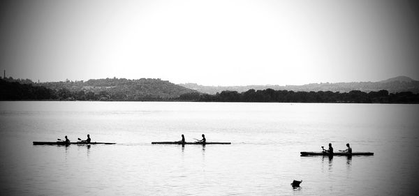 People sculling in lake against sky