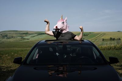Man wearing horse mask standing in car