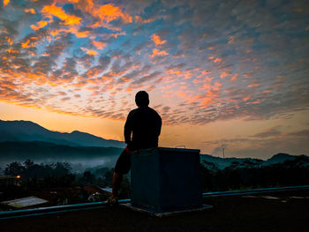 Rear view of silhouette man standing on mountain against sky