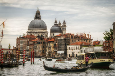 Boats in canal by buildings against sky in city