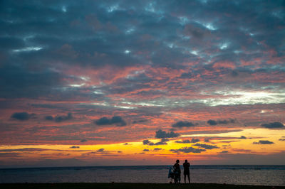 Silhouette people on beach against dramatic sky during sunset