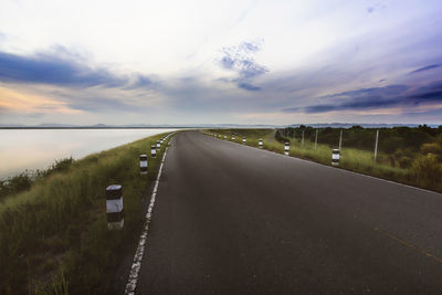 Empty road amidst field against sky during sunset