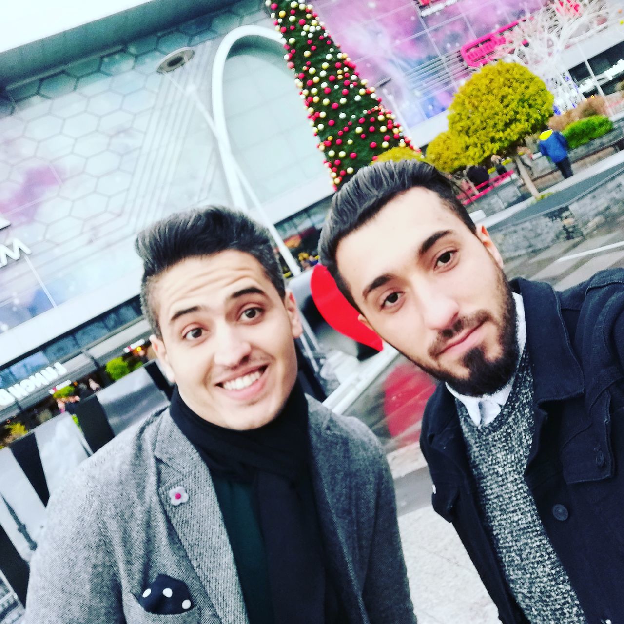 portrait, two people, young men, smiling, looking at camera, young adult, real people, headshot, togetherness, men, people, lifestyles, emotion, front view, happiness, clothing, architecture, bonding, casual clothing, couple - relationship, warm clothing, positive emotion, scarf