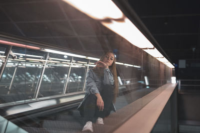 Portrait of woman sitting on escalator in city at night