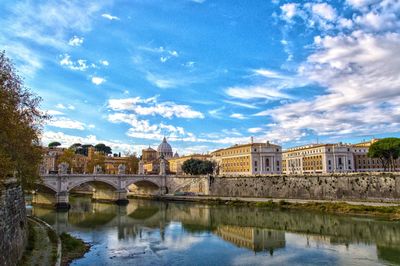 Bridge over river by buildings against sky