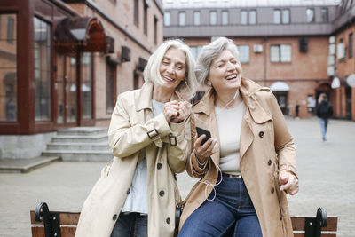 Cheerful female friends listening music while sharing headphones