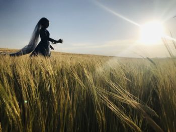 Side view of woman holding crop walking on field