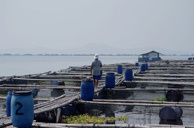 Rear view of man walking on bamboos over lake